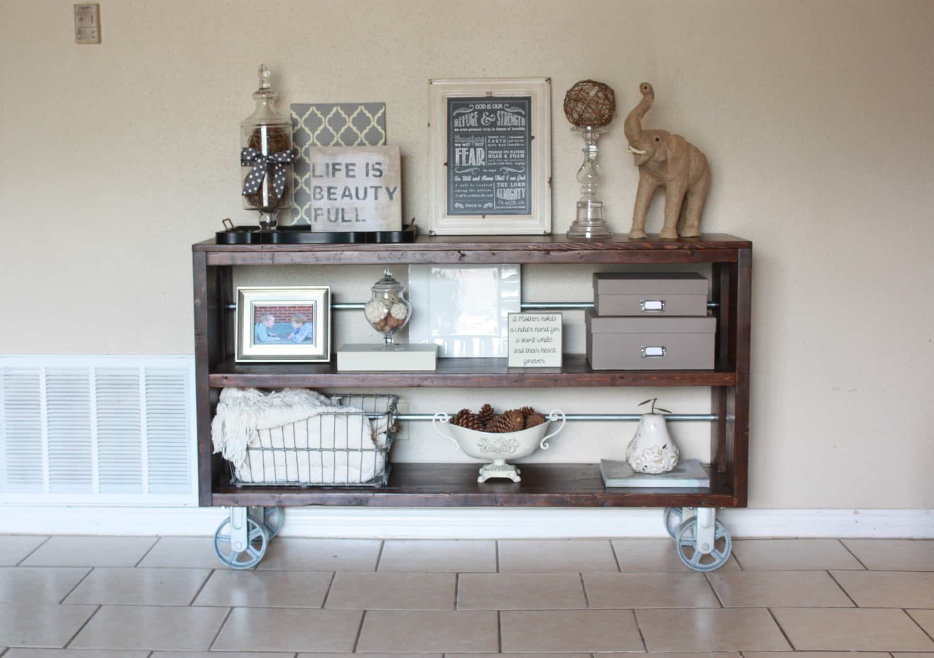 Beautiful dark wood and steel console table with big metal wheels and decorated with gray and white decor 