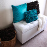 Upholstered storage bench with turquoise and brown pillows on it