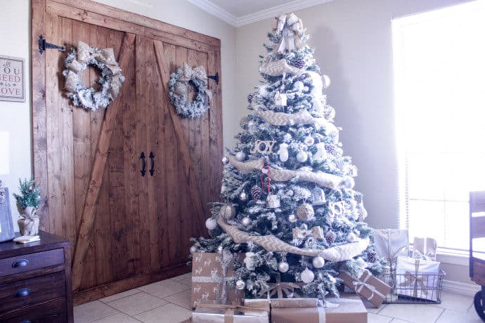 Flocked Christmas tree and wreaths hanging on barn door and presents are under the tree