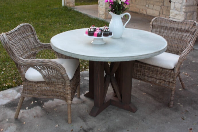 view of the concrete tabletop of the round outdoor dining table with wicker chairs and flowers and cupcakes on the table