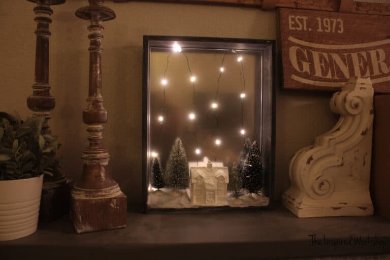 DIY Christmas Shadow Box with fairy lights on with a white house and bottle brush trees