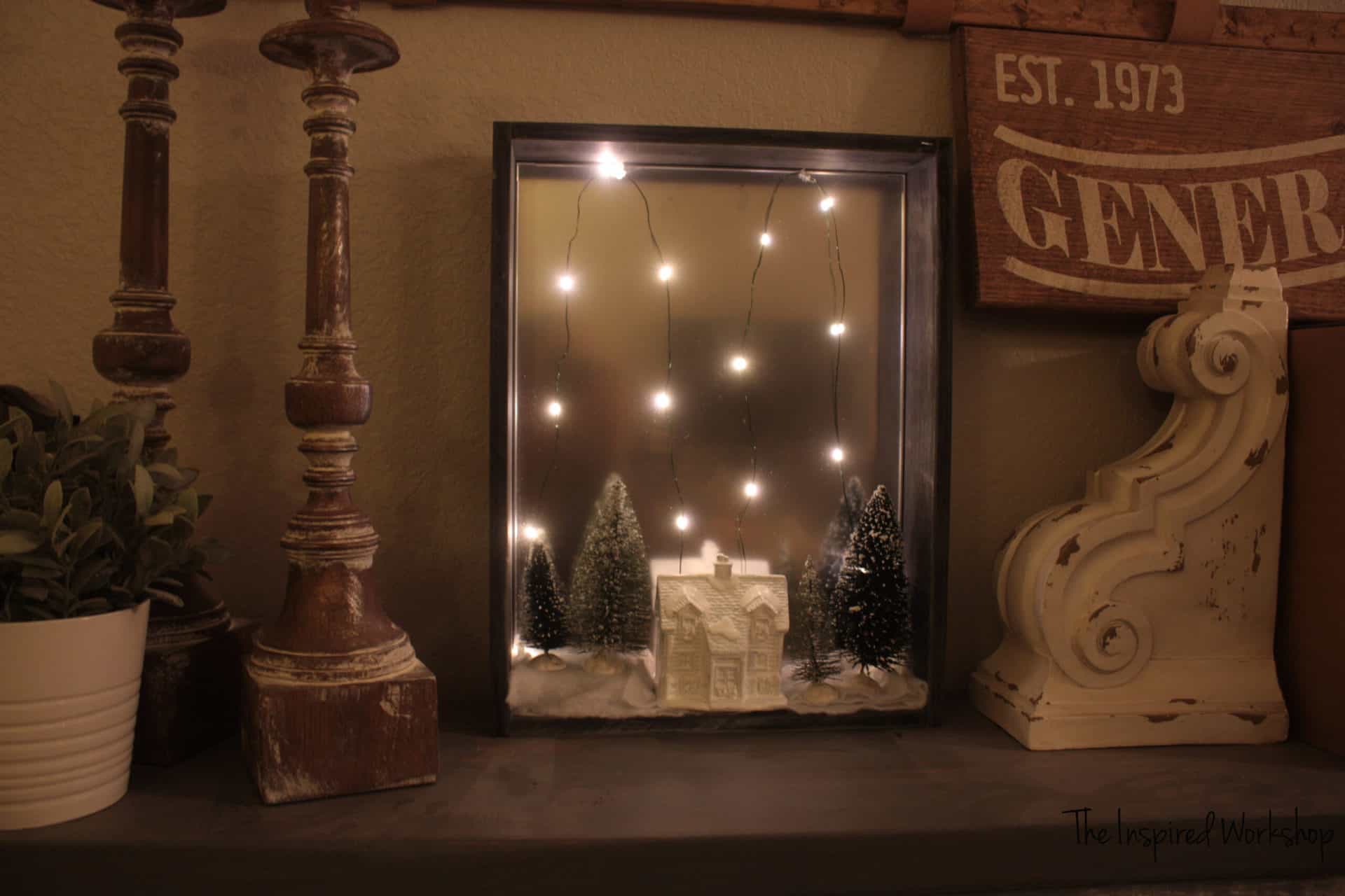 DIY Christmas Shadow Box with fairy lights on with a white house and bottle brush trees