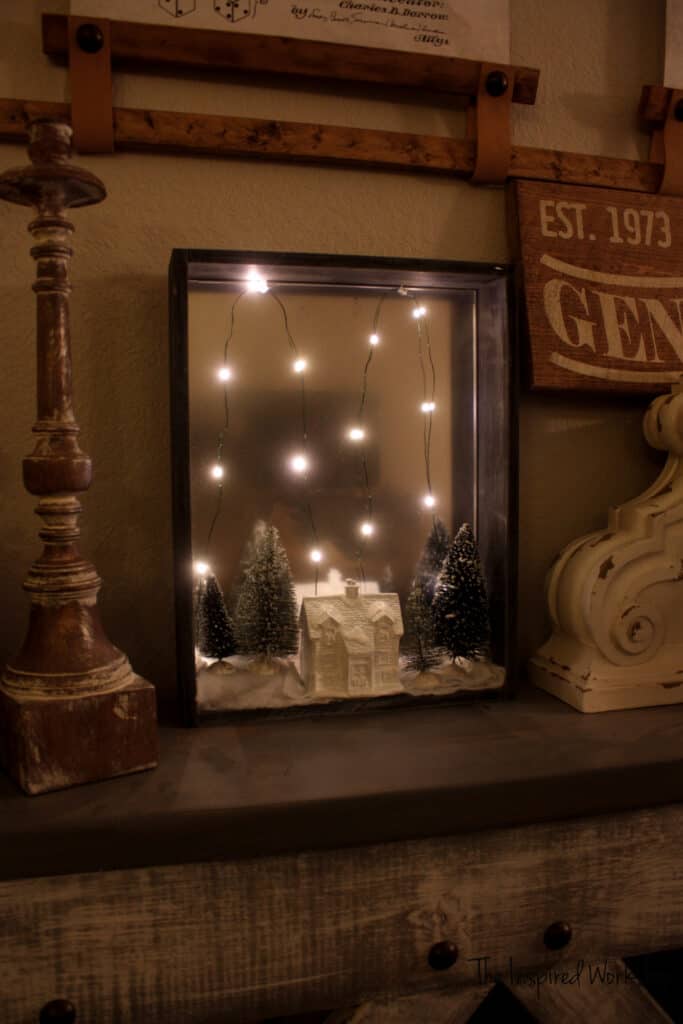 DIY Shadow Box with white ceramic house and bottle brush trees with fairy lights