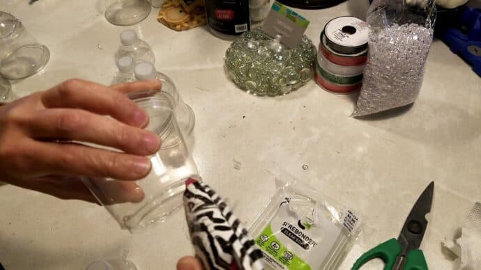 Adding hot glue to the cup to attach the water bottle top to make the bells