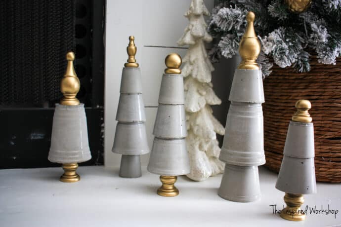 Five christmas trees made out of concrete and topped with gold wooden finials