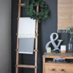 Blanket ladder proped against the wall with a wreath over one side and two blankets a nightstand to the right