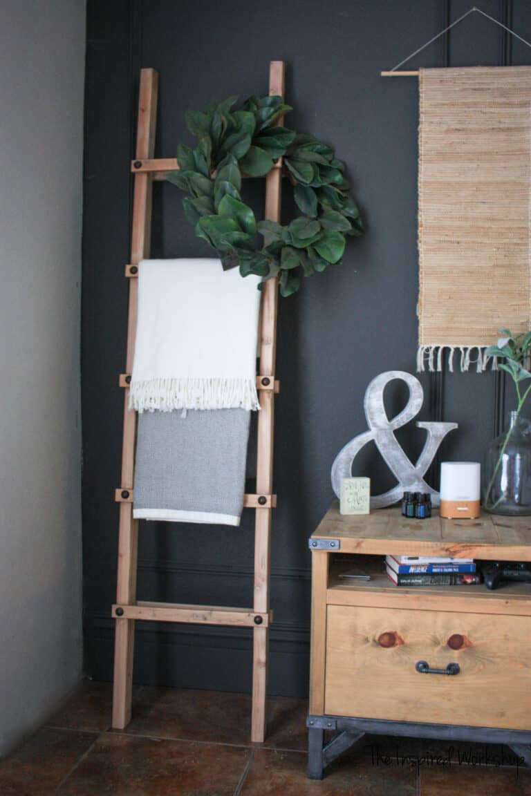 Blanket ladder proped against the wall with a wreath over one side and two blankets a nightstand to the right