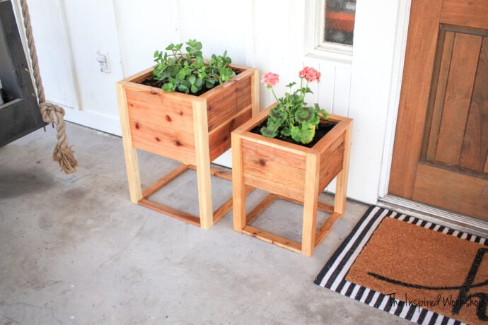 Planter Boxes sitting by the front door with a balck and white striped rug and plants inside the planters