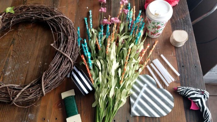 All the supplies for the spring wreath laid out - grapevine wreath form, flowers, floral wire, hot gule gun and a metal heart