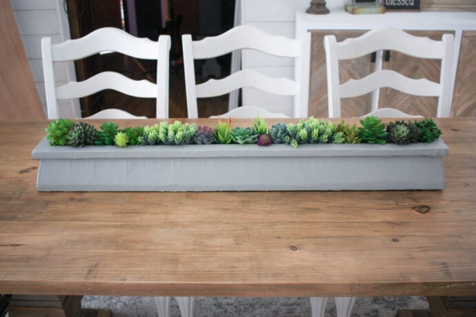 DIY Succulent Table Centerpiece sitting in the middle of the table with white chairs