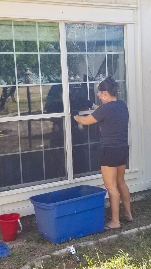 girl removing broken shards of glass from window that is being replaced