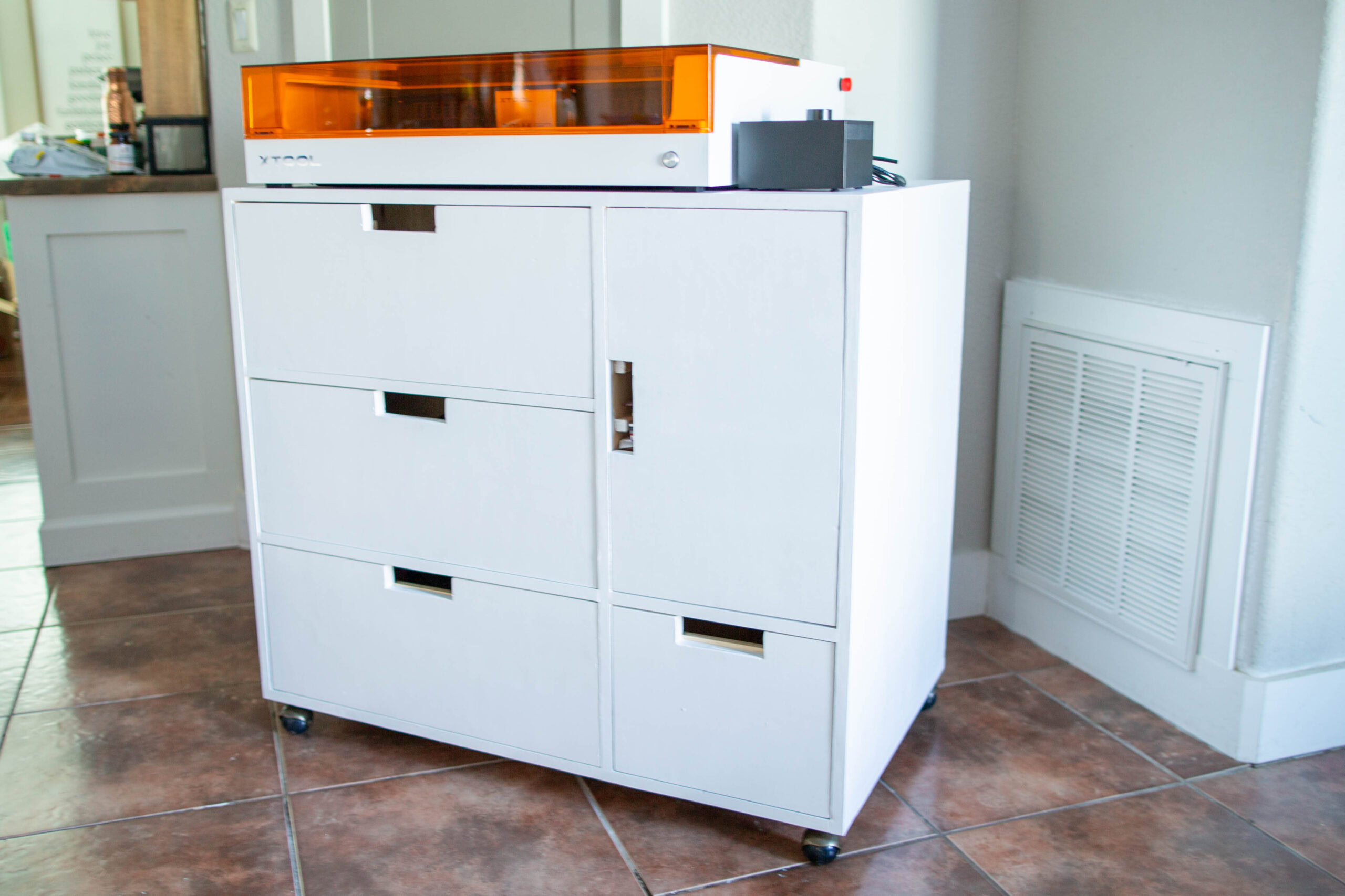 craft storage cart - white cart with four drawers and one door with the xtool S1 laser engraver sitting on top of the cart.