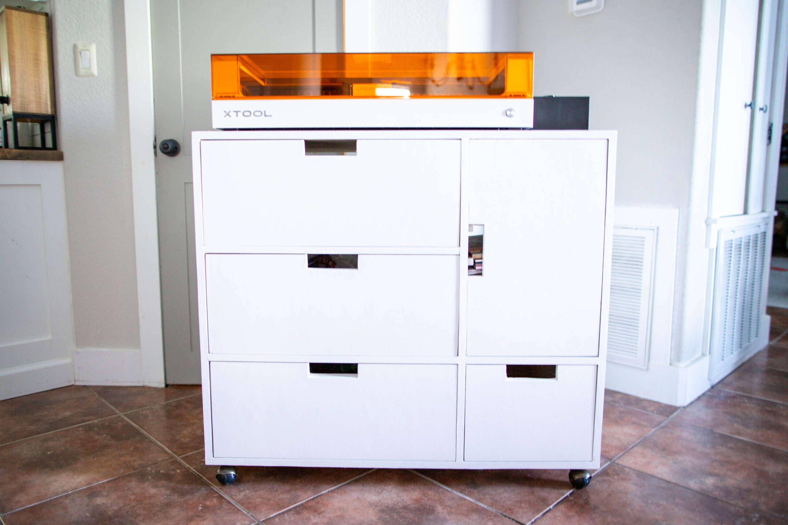 white storage cart with laser engraver on top - three drawers on the left and one door on top of a drawer to the right.
