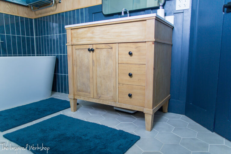 light wood bathroom vanity with navy blue walls behind it and dark blue rug in front of it.