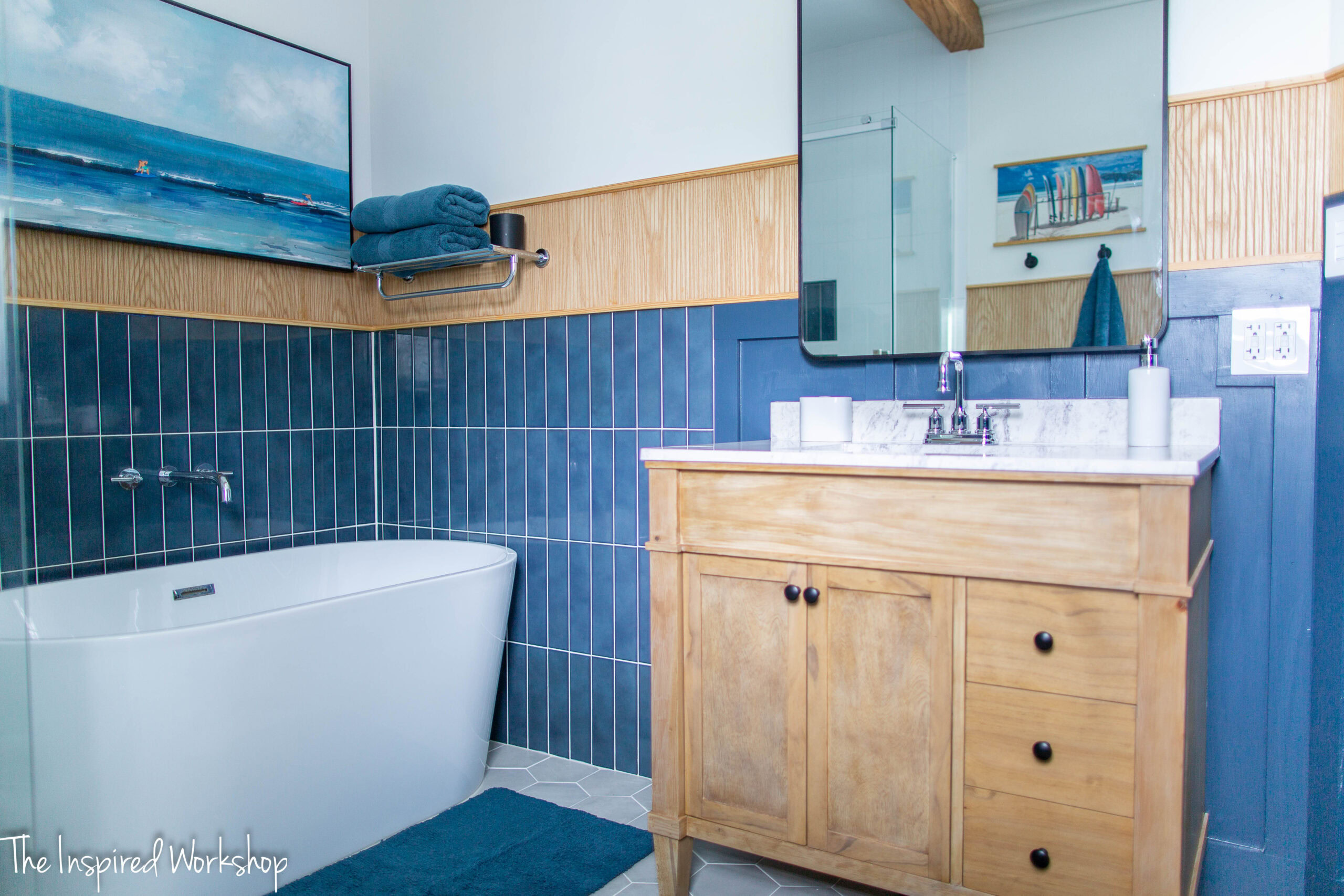 Bathroom showing a light wood vanity, a white bathtub and some surfing wall art above the bathtub