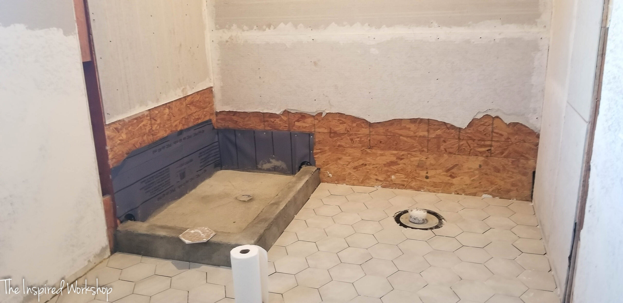 Shower pan in progress, the shower pan liner is still visible and there is a layer of concrete over the liner.