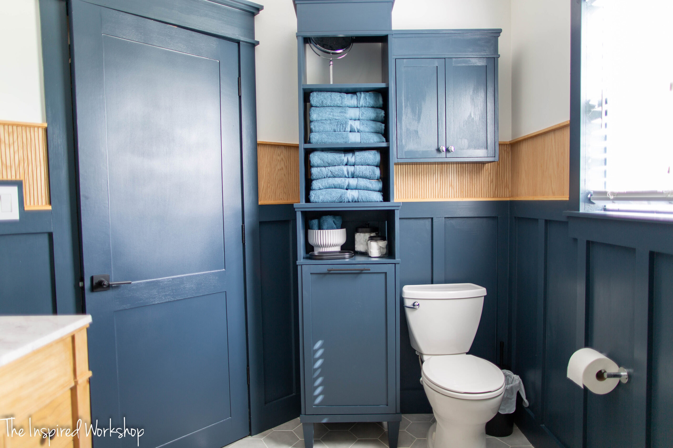 navy blue bathroom with a view of the toilet and laundry hamper with shleves