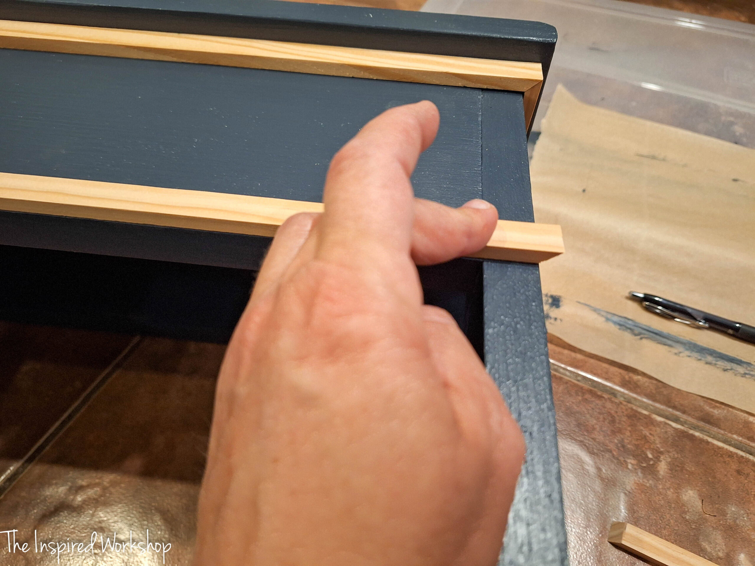adding trim to the cabinet showing a finger holding the trim in place while glue dries