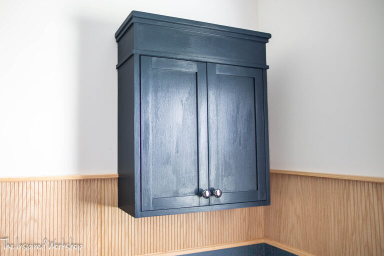 Navy blue cabinet that sits over the back of the toilet with two doors.